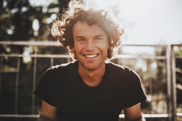 Outdoor closeup portrait of handsome freckled smiling male with curly hair, posing for social advertisement, in the city street on sunset sunlight with copy space for your promotional information